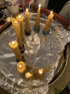 a group of 9 tall yellow homemade candles burning on a piece of foil